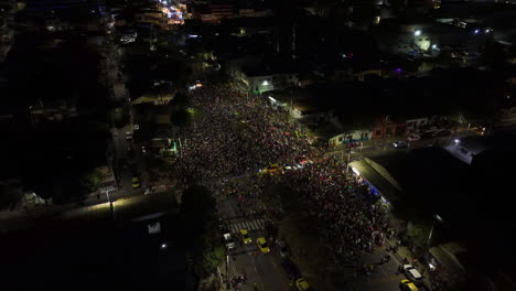 Aerial-view-around-a-street-full-of-people-celebrating-the-Carnival-of-Barranquilla,-night-in-Colombia