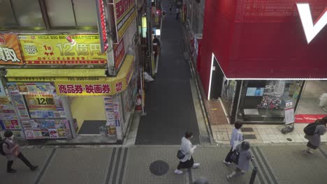 High-Angle-View-Looking-Down-At-People-Walking-Across-Pavement-With-Narrow-Street-Leading-Off-It-In-Shinjuku,-Tokyo