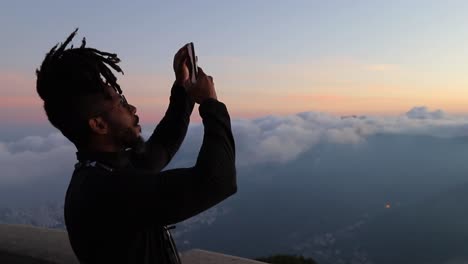 Schwarzer-Tourist-Blickt-Auf-Wolken,-Die-über-Der-Stadt-Rio-De-Janeiro-Schweben,-Und-Klickt-Auf-Fotos-Im-Smartphone,-Seitenprofil,-Mittlere-Nahaufnahme