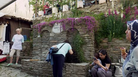 Woman-washes-hands-and-drinks-from-Turkish-village-stone-water-fountain