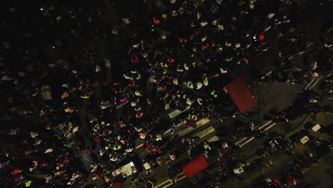 Aerial-view-above-people-celebrating-the-Batalla-de-Flores,-on-dark-night-streets-of-Barranquilla,-Colombia---screwdriver,-drone-shot