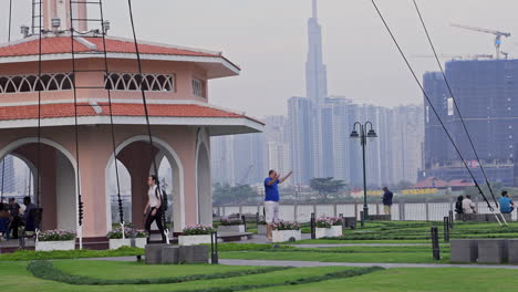 Un-Hombre-Haciendo-Ejercicio-En-Un-Parque-En-El-Distrito-1-De-La-Ciudad-De-Ho-Chi-Minh,-Con-El-Emblemático-Edificio-81-Y-El-Río-Al-Fondo.