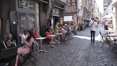 Ein-Junger-Mann-Geht-Durch-Die-Gepflasterte-Straße-Mit-Vieux-Touren,-Während-Menschen-Auf-Zahlreichen-Kleinen-Terrassen-Auf-Der-Straße-Sitzen