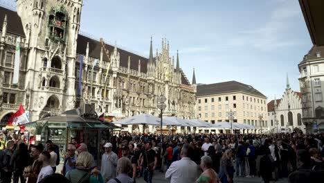Slow-motion-shot-of-crowd-of-tourists-walking-around-famous-Rathaus-Glockenspiel-in-Marienplatz,-Munich-on-a-sunny-day