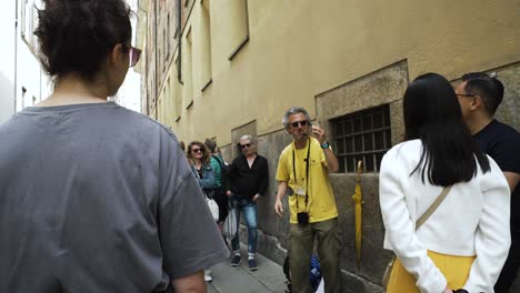 Energetic-Italian-Tour-Guide-Speaking-Enthusiastically-To-Tourists-In-Narrow-Street-In-Milan,-Italy