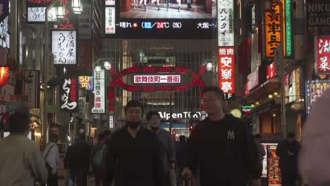 Japanese-Locals-Walking-Past-With-View-Of-Flashing-Red-LED-Signboard-Of-Kabukicho-Street-In-Shinjuku-At-Night-In-Background