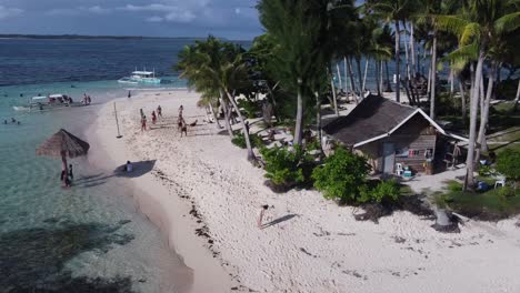 People-on-holiday-swimming,-relaxing-and-playing-beach-Volleyball-on-white-sand-of-small-tropical-Guyam-Island,-Siargao
