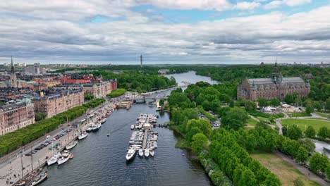 Djurgaarden-bridge-and-water-channels-in-central-Stockholm-Sweden---Beautiful-summer-day-aerial-during-a-busy-day-with-boats-on-water-and-cars-and-people-in-the-streets---60-Fps