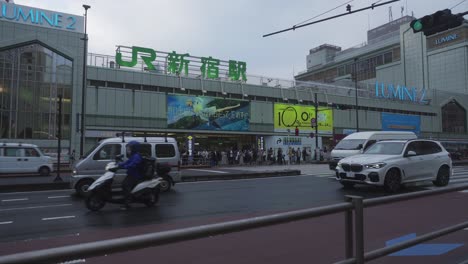 Blick-Von-Der-Anderen-Straßenseite-Auf-Den-Verkehr,-Der-An-Einem-Bewölkten-Tag-In-Tokio-Am-Bahnhof-Shinjuku-Vorbeifährt