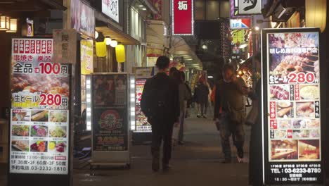 Einheimische-Gehen-Die-Shinjuku-Straße-Entlang,-Vorbei-An-Restaurants,-Deren-Menüs-Abends-Beworben-Werden