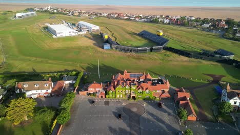 Preparativos-Para-El-Abierto-De-2023-En-El-Club-De-Golf-Royal-Liverpool,-Wirral,-Reino-Unido:-Casa-Club-Con-Drones-Aéreos-En-El-Sentido-De-Las-Agujas-Del-Reloj-Desde-Lejos,-Revelación-Del-Campo-Y-El-área