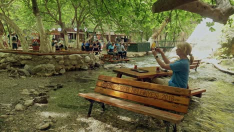 Eine-Frau-Fotografiert-Die-Umgebung-Der-Saklikent-Schlucht-Vom-Picknicktisch-Im-Fluss-Aus