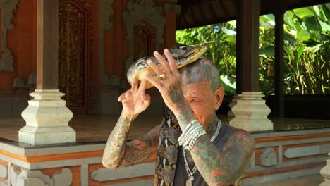 Toma-En-Cámara-Lenta-De-Un-Encantador-De-Serpientes-Tradicional-En-Un-Templo-Balinés-Con-Una-Serpiente-Alrededor-Del-Cuello-Y-Controlándola-Elegantemente