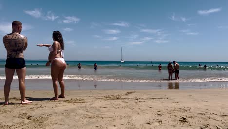 Footage-of-a-pregnant-woman-on-the-beach-rubbing-her-bump-in-sepia-or-film-burn-color-with-catamaran-in-background