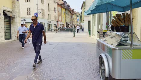 Street-vendor-with-idea-cream-cart-and-pedestrians-on-street-of-Annecy,-summer-in-France