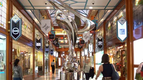 Shoppers-window-shopping-at-iconic-Brisbane-arcade,-shopping-galleria-in-heritage-listed-building-in-Queen-Street-Mall,-static-shot-capturing-Mirage-sculpture-by-Gidon-Graetz-as-the-centrepiece