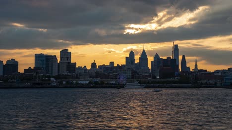 Eine-Zeitrafferansicht-Der-Skyline-Von-Philadelphia-Mit-Dem-Sonnenuntergang-Dahinter-Und-Dem-Fluss-Im-Vordergrund