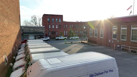 Drone-view-of-a-mail-delivery-van-in-the-parking-lot-of-a-post-office-with-an-American-flag-flown-at-half-staff-at-sunset