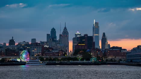 Eine-Zeitrafferansicht-Der-Skyline-Von-Philadelphia-Mit-Dem-Sonnenuntergang-Dahinter-Und-Dem-Fluss-Im-Vordergrund