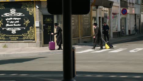 Two-Orthodox-Jews-walking-with-travel-trolleys-on-wheels-in-the-city-street-of-the-Antwerp's-diamond-district,-Belgium
