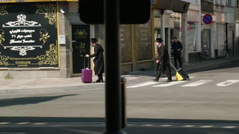 Zwei-Orthodoxe-Juden-Laufen-Mit-Reisetrolleys-Auf-Rädern-Durch-Die-Stadtstraße-Im-Diamantenviertel-Von-Antwerpen,-Belgien