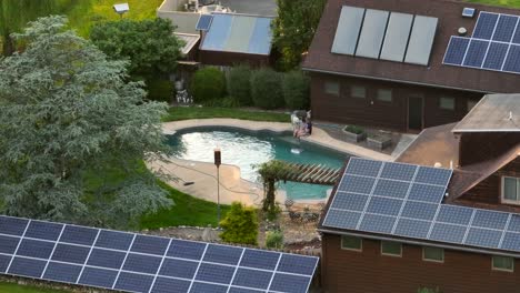 Aerial-shot-of-house-roof-covered-with-solar-panels-and-a-swimming-pool-in-the-middle-and-two-people-with-dogs