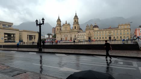 Menschen,-Die-Bei-Regen-In-Der-Innenstadt-Mit-Dem-Justizpalast,-Der-Nationalhauptstadt-Und-Der-Kathedrale-Von-Bogotá-Spazieren?
