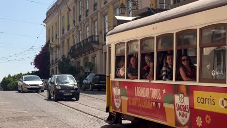 Establishing-shot-of-passing-traditional-yellow-tram-on-railroad-in-Lisbon-City-during-bright-sunny-day-in-old-town---Close-up-slow-motion