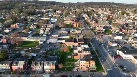 Panoramic-drone-view-of-a-downtown-district-and-outlaying-neighborhoods-with-tree-filled-hills-in-the-background-in-the-springtime-at-sunset