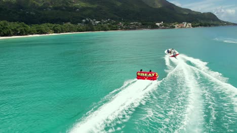 Tourist-couple-having-a-donut-ride-at-the-Watersport-at-the-beau-vallon-beach,-beautiful-sunny-day-and-calm-sea,-Mahe-Seychelles-2