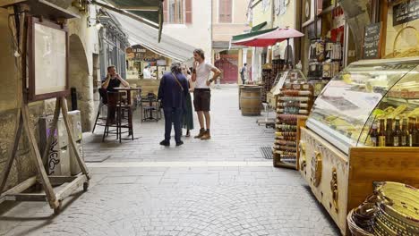 Cobbled-street-in-medieval-Annecy-farmers-market-with-cheese-and-home-produce,-a-cafe-and-pedestrians