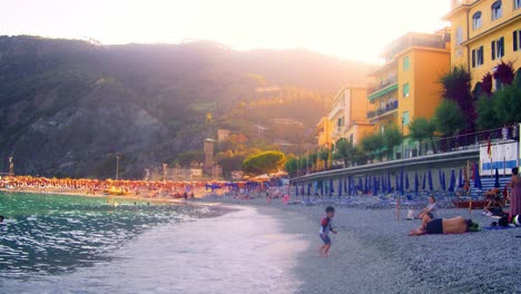 Hermosa-Playa-En-Italia-Al-Atardecer-Con-Niños-Jugando-Y-Turistas-Y-Lugareños-Italianos-Relajándose-En-Una-Colorida-Ciudad