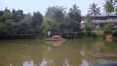 A-man-skillfully-pulls-on-a-rope,-guiding-a-bamboo-raft-across-a-murky-pond-with-passengers-onboard