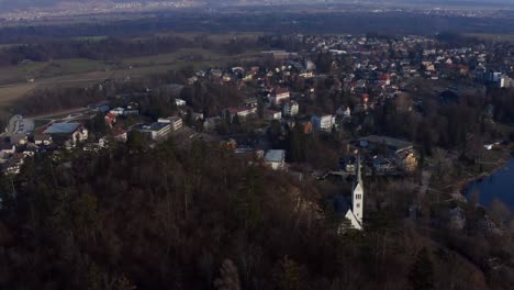 Nach-Unten-Geneigter-Luftblick-über-Die-Stadt-Bled-Und-Die-Kirche-Am-Seeufer-Mit-Bergen-Im-Hintergrund-In-Slowenien