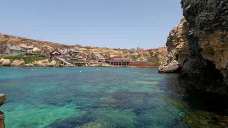 Clear-ocean-waters-reveal-large-boulders-below,-seafront-luxury-homes-on-island-of-malta