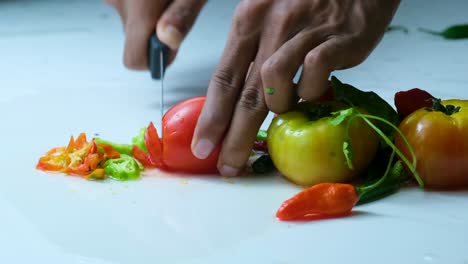 Koch-Schneidet-Rote-Tomaten-Auf-Einer-Weißen,-Mit-Chilischoten-Und-Anderen-Tomaten-Bedeckten-Oberfläche