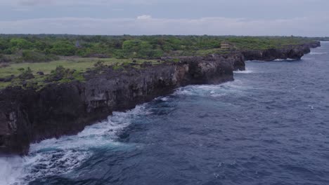 Drone-flies-along-clif-with-small-waves-at-Sumba-Indonesia,-aerial