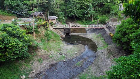 Aerial---Forward-drone-of-footbridge-over-shallow-stream-in-forest-settlement