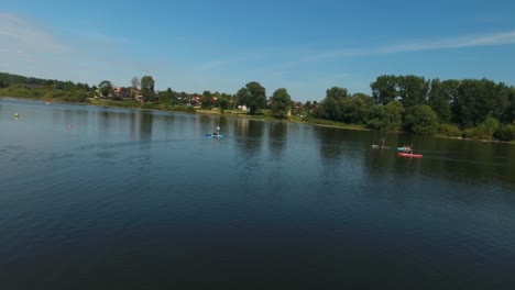 People-enjoying-summer-vacations-by-stand-up-paddleboarding-on-a-lake-in-Poland,-under-beautiful-weather,-captured-in-a-dynamic-4K-drone-shot