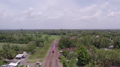 Drone-follows-red-train-at-Jogjakarta-Indonesia-during-day-time,-aerial