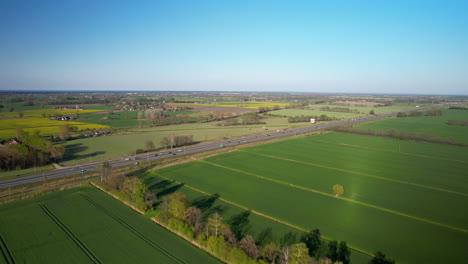 Bustling-road-with-fast-moving-vehicles-in-green-fields-countryside-landscape