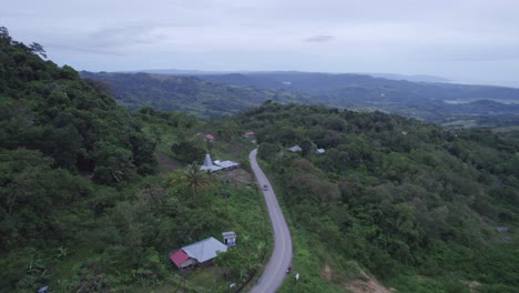 Car-drives-at-small-road-with-houses-on-side-at-Sumba-island-Indonesia,-aerial