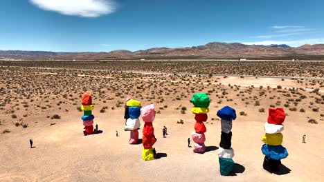 Seven-Magic-Mountains-Rock-Sculpture-by-Ugo-Rodinone-in-South-Las-Vegas,-aerial-rising-on-hot-sunny-day