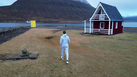 Man-Walking-at-Mjóeyri-Cottages-in-Iceland,-Drone-Follow-Me,-Behind