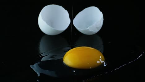 Huevo-De-Pato-Resquebrajado-En-Una-Superficie-Reflectante-Negra,-El-Yugo-Gotea-Desde-Fuera-De-La-Pantalla