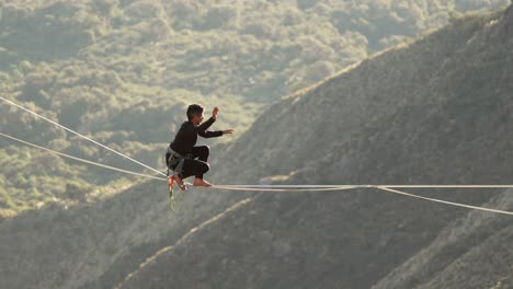 Man-standing-up-on-a-highline-at-sunset-with-defocused-background-and-valley-below-at-high-altitude