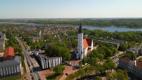 Aerial-shot-of-the-city-church-Siauliai,-Cathedral-of-Saints-Peter-and-Paul,-on-a-sunny-day-by-the-river-Siauliai,-Lithuania,-zoom-in