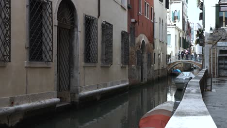 Traditionelle-Venezianische-Häuser-Neben-Einem-Schmalen-Kanal-In-Venedig-Mit-Einer-Brücke-Im-Hintergrund