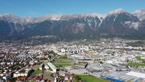 Innsbruck-in-a-panoramic-vertical-aerial-view-on-a-sunny-day-full-of-autumn-tranquility-with-a-green-alpine-forest-and-a-blue-sky-and-the-alps-in-the-background-with-its-peaks-in-Tyrol-in-Austria