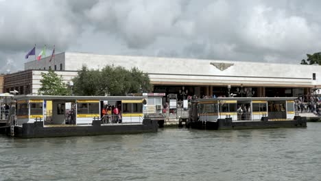 Ferry-boats-in-front-of-a-busy-Venezia-Santa-Lucia-railway-station,-the-background-fill-with-people-travelling-to-the-beautiful-European-city-of-Venice-on-a-grey-gloomy-day,-Italy